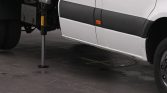 White van with a metal support leg deployed to the side, resting on a circular foot on pavement.