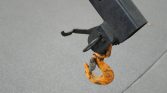 Close-up of an orange towing hook on a black trailer hitch against pavement.