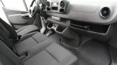 Interior of a black-cloth front cabin in a van, showing the driver’s seat, steering wheel, and dashboard with cupholders and storage areas