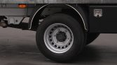 Rear wheel of a dump truck with silver rim and black tire, under a gray cargo bed with white fender trim and an orange reflector nearby.
