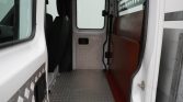 Interior of a white cargo van with a diamond-plate metal floor, a wooden divider on the right, and the rear door opening visible from the side entry.