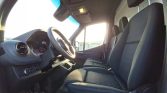 Interior view of a van cab showing the steering wheel, dashboard, and two front seats bathed in sunlight from the side window, with a clear view of the driver's area.