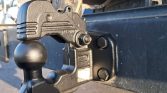 Close-up of a trailer hitch with a ball mount attached to a blue trailer frame, showing the bolt and pin.