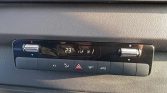 Car climate control panel with temperature set to 23°C, two rotary dials on ends, and a row of function buttons (A/C, defrost, hazard, air circulation) in a black dashboard panel