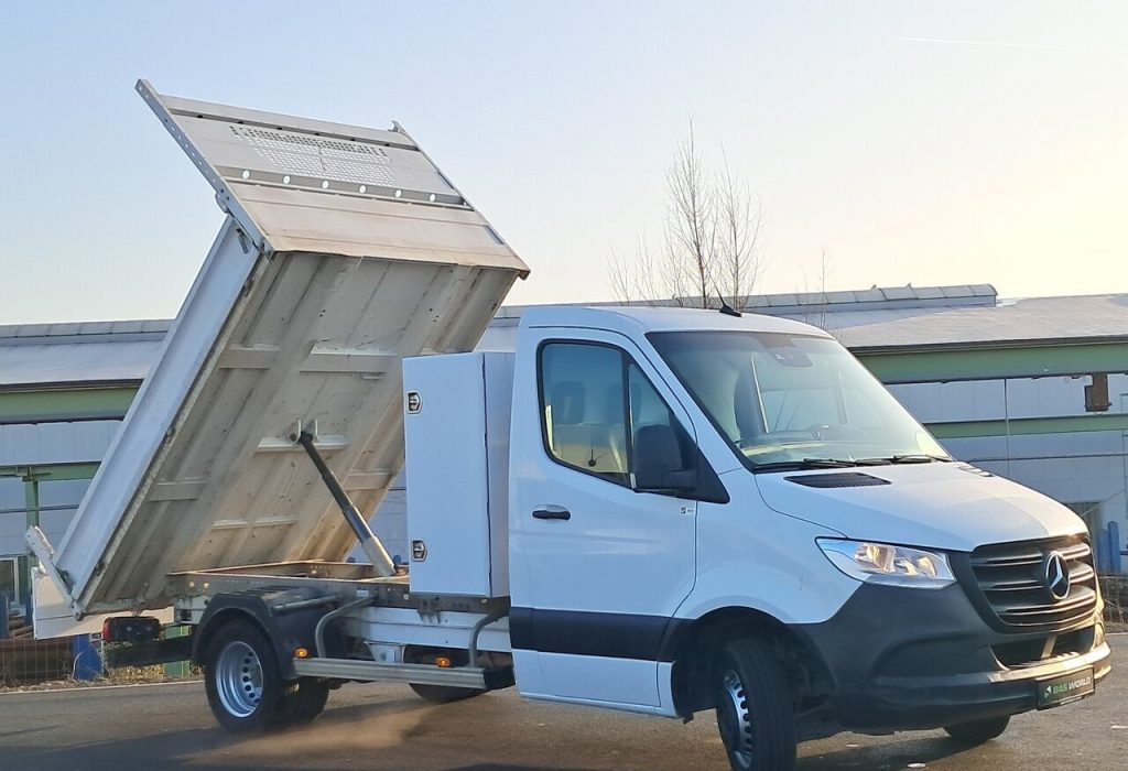 White Mercedes-Benz dump truck with its cargo bed raised for unloading at an industrial site.