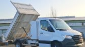 White Mercedes-Benz dump truck with its cargo bed raised for unloading at an industrial site.