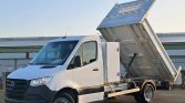 White Mercedes-Benz tipper truck with raised cargo bed ready to unload at a site