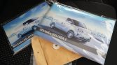 Two Maxus vehicle brochures featuring white vans on a blue cityscape background with the text 'MAXUS e DELIVER 3' visible, resting on a car seat.
