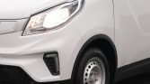 White van front-left with illuminated headlight, grille area, and steel wheel visible at the front corner.