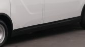 Side view of a white van showing the sliding door, wheel, and black lower trim on asphalt road.