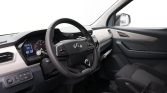 Cockpit view of a modern car interior from the driver's side, showing the steering wheel, dashboard, and front seats with black upholstery and white stitching.