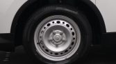 Close-up of a silver steel wheel with lug nuts and a black tire on a white vehicle, showing the wheel well and tire treads.