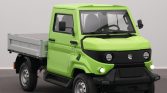 Front three-quarter view of a bright lime-green utility pickup truck with a flatbed, black bumper and round headlights, indoors.