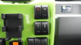 Close-up of a bright green vehicle dashboard with hazard and defrost buttons, a phone holder on the left, and an orange 21°C climate display below.