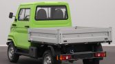 Rear-left view of a bright green compact pickup with a silver flatbed cargo area, shown indoors in a studio setting in full side profile tilt.