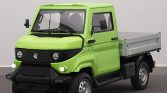 Bright green compact utility truck with a silver flatbed, black bumper, and large side mirrors, parked indoors.