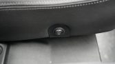 Round car-seat heater switch with heat-wave icon on black trim, located at the lower side of the seat