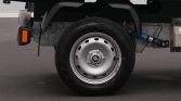 Rear wheel of a flatbed/utility truck showing a silver steel rim, black tire, and undercarriage components including an orange side marker.