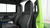 Two dark gray front seats in a vehicle, with the bright green door frame visible on the right and the seat belt hanging to the side, interior view from the passenger side.