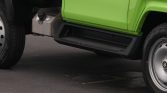 Close-up of a bright green truck side with a metal fuel tank and black step undercarriage near the front wheel.