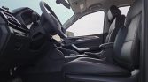 View of the car's front cabin from the driver's side, showing a black steering wheel, dashboard, and front seats with red stitching.