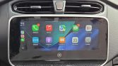 Car infotainment touchscreen showing colorful app icons (Phone, Music, Maps, Messages) in a car interior window.