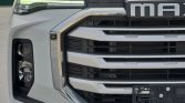 Front view of a white heavy-duty truck, highlighting the chrome grille and left headlight assembly with LED daytime running lights.