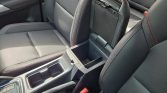 Center console of a car with open storage and cup holders between front seats, red stitching visible on seats and armrest edges.