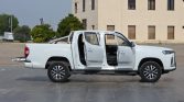 White pickup truck with all four doors open, parked on a paved lot near a beige building