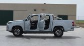 White four-door pickup truck with all doors open, parked on a concrete lot by a beige industrial building.