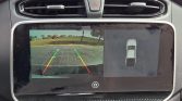 Car infotainment screen showing rear-view camera with colored parking guidelines (green/yellow/red) and a top-down car diagram on the right for parking assist, in-dash display mode.