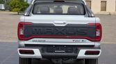 Rear view of a white Maxus T50 EV pickup with a chrome roll bar, large 'MAXUS' lettering on the tailgate, and red-accent taillights forming a continuous line across the back.