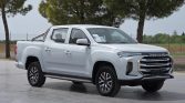 White Maxus pickup truck parked outdoors on a paved lot with trees in the background, front three-quarter view.