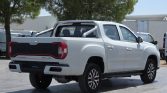 Rear three-quarter view of a white double-cab pickup truck with a metal roll bar in the bed, parked outdoors under trees.