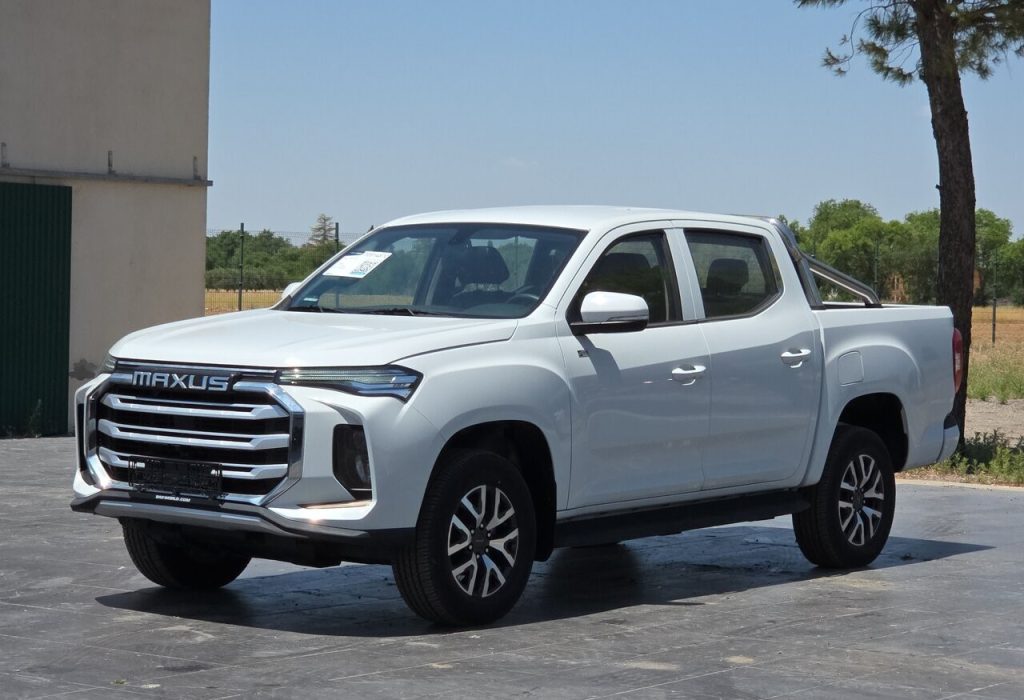 Front three-quarter view of a white Maxus pickup truck with a bold chrome grille and crew cab on a paved lot.
