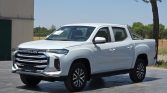 Front three-quarter view of a white Maxus pickup truck with a bold chrome grille and crew cab on a paved lot.