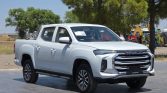 Front-three-quarter view of a white Maxus pickup truck parked on a paved lot with trees in the background.