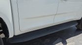 White vehicle with a black side running board; small dent and scratches along the lower door panel, near the wheel arch.