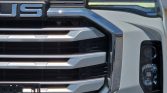 Close-up of a modern white pickup truck's front end, featuring a chrome grille and LED daytime running lights across the top alongside the right headlight.