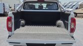 Open pickup truck bed with tailgate down, showing a clean, ribbed bed liner and a metal roll bar behind the cab in a parking lot.