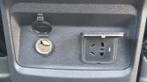 Car interior panel with an open 12V cigarette lighter socket (left) and a built-in universal power outlet with a hinged cover (right).