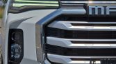 Close-up of a white pickup truck's front grille and left headlight with chrome trims.