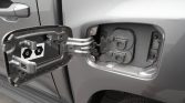 Open fuel filler door on a gray vehicle, showing the empty filler neck and internal locking components.