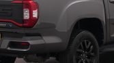 Rear half of a gray pickup truck showing a red tail light, rear bumper, and a black alloy wheel with tire on the right side.