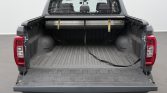 Open cargo bed of a gray pickup with tailgate down, showing a lined bed and straps along the top edge.
