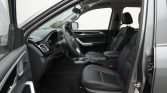 Front interior of a modern car shown from the open driver's side door, featuring black leather seats and a steering wheel with red stitching.
