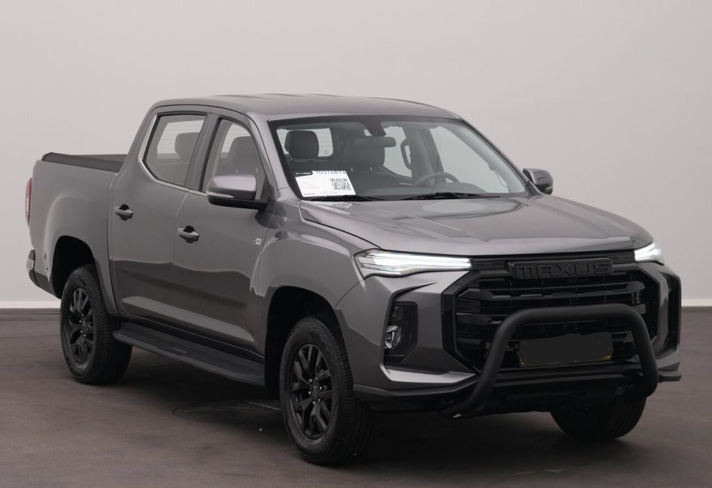 Gray Maxus pickup truck with bull bar and crew cab, parked indoors in a showroom.