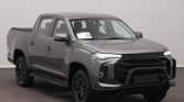 Gray Maxus pickup truck with bull bar and crew cab, parked indoors in a showroom.