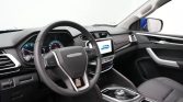 Interior of a modern car cabin with a leather steering wheel and digital instrument cluster, center touchscreen displaying a blue car image, and gear selector nearby