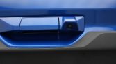 Close-up of a blue car door handle with a small integrated camera beside it, likely a backup/door camera.